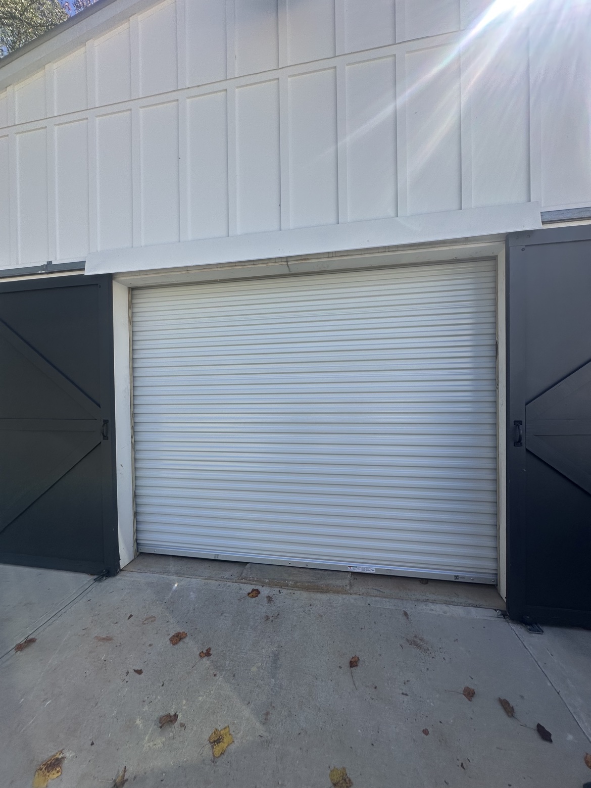 White roll-up door installed between dark sliding doors on a barn-style building